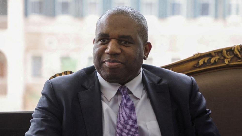 David Lammy with short dark hair wearing a grey suit and purple tie