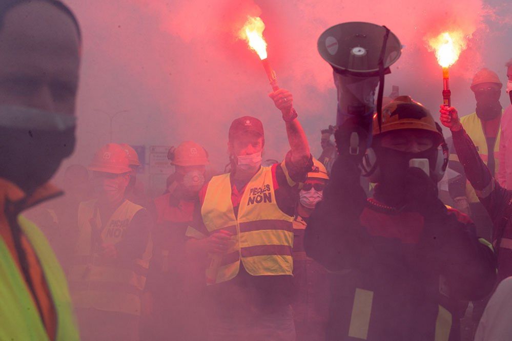 People in fluorescent jackets hold burning flares