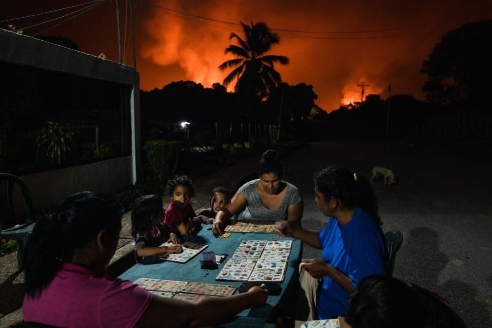 Neighbours play Animal Lotto under a sky lit by one of the world's largest gas flares, Punta de Mata, Venezuela, 5 November 2022