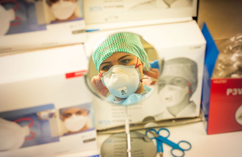 A health worker puts on her mask while looking in the mirror