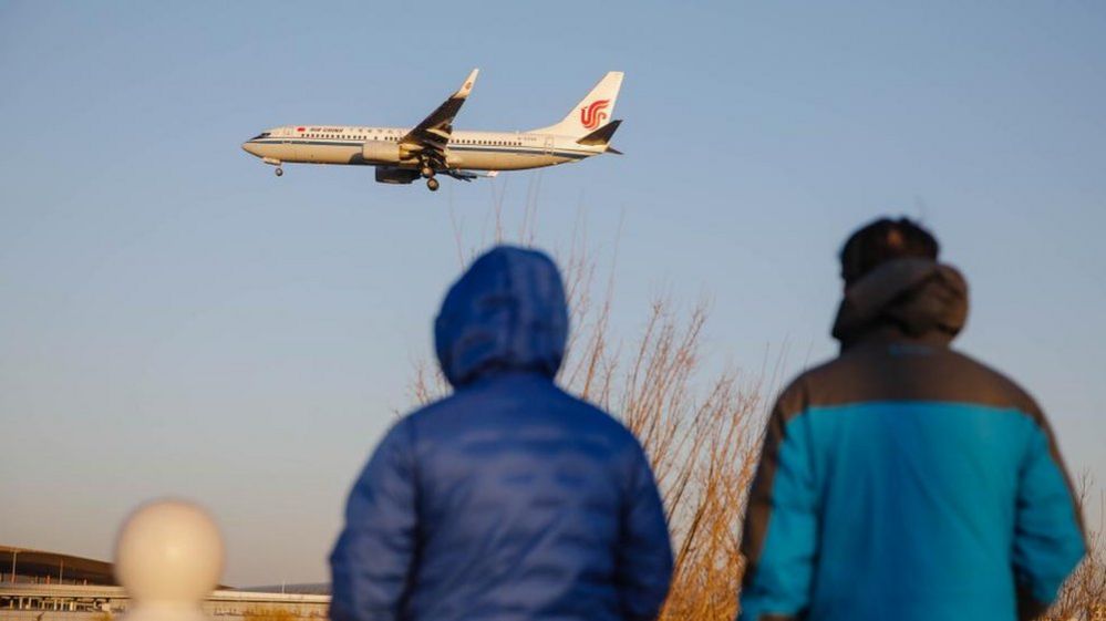 People watch a passenger plane landing at Beijing International Airport