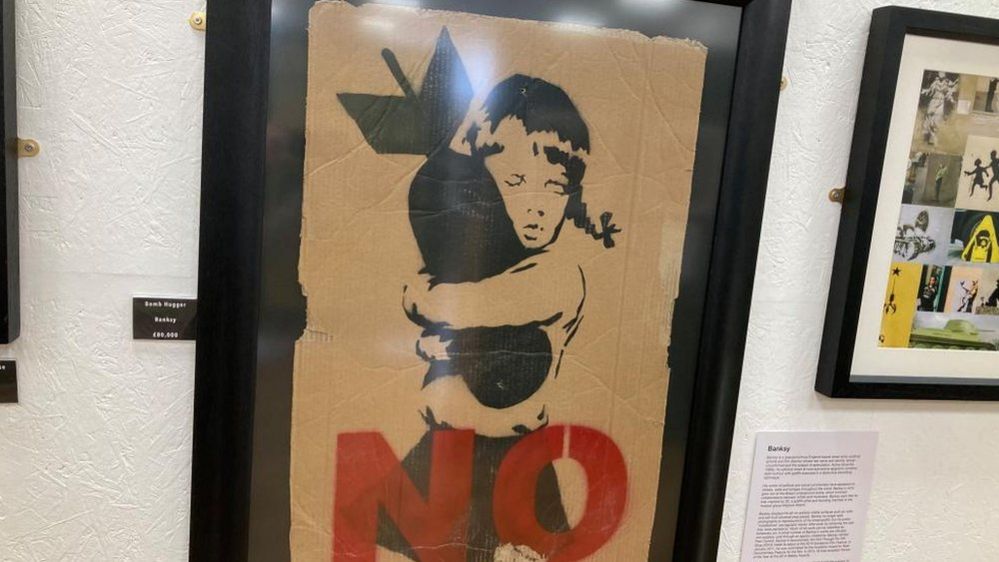 Painting of a child hugging a bomb with the word "NO" in red letters at the bottom