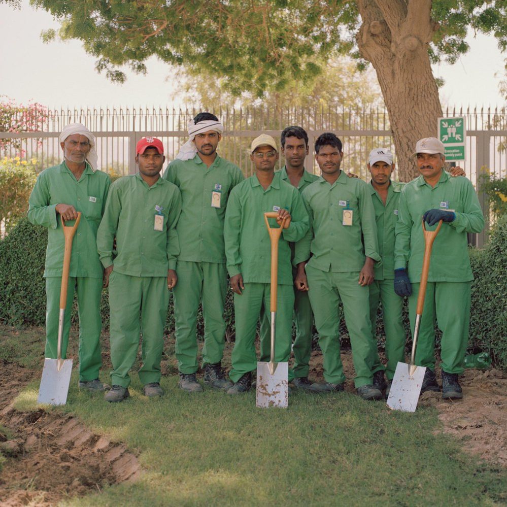 A group of men outdoors, dressed in green and holding spades