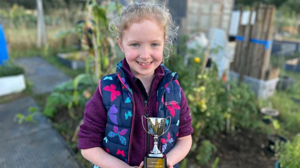 Penny holding her trophy in a purple fleece in her allotment