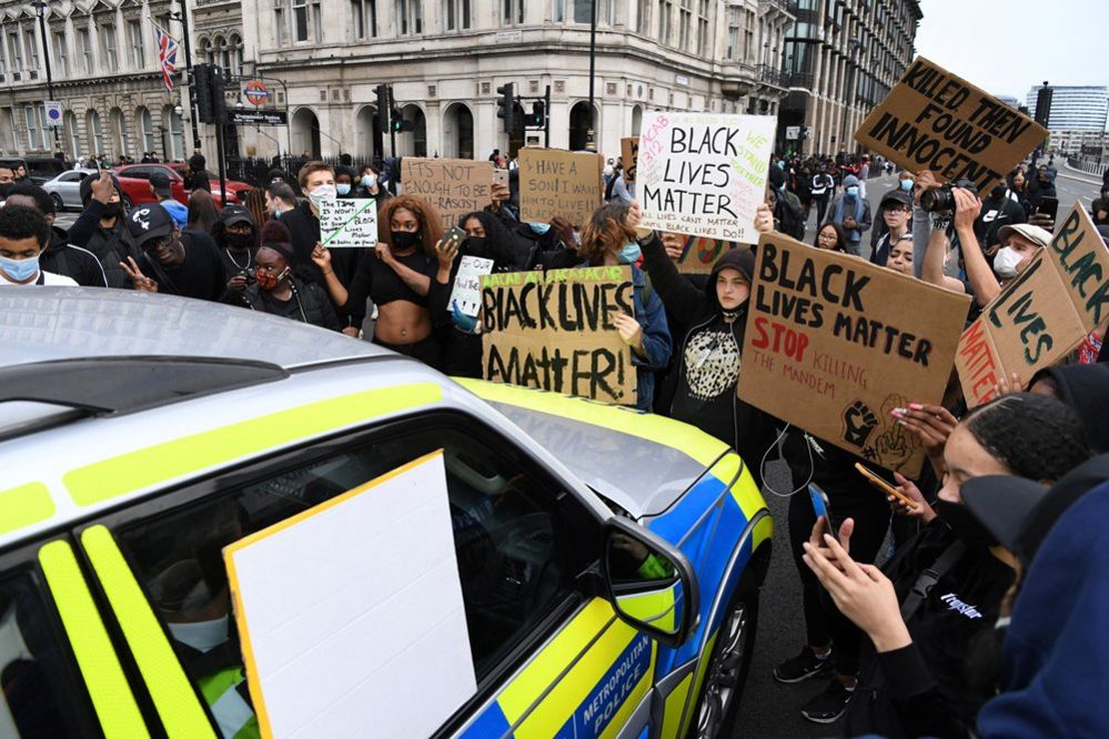 Protestors with placards gather around a police car