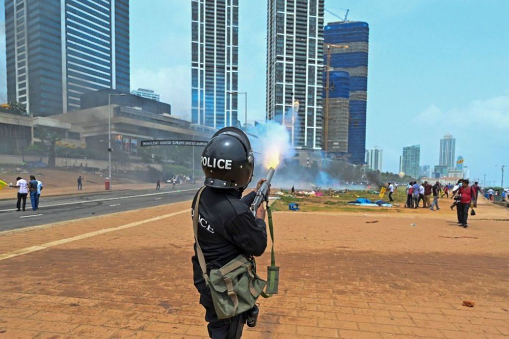 A policeman fires tear gas during a clash between government supporters and demonstrators outside the President's office in Colombo