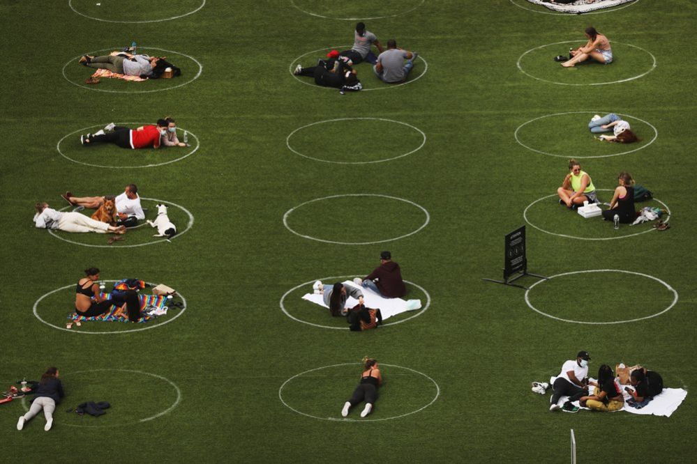An aerial view showing people relaxing in a park whilst staying designated white circles to ensure social distancing