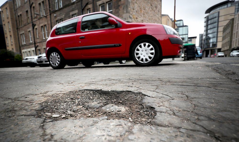 A pothole in a road with a red car in the background