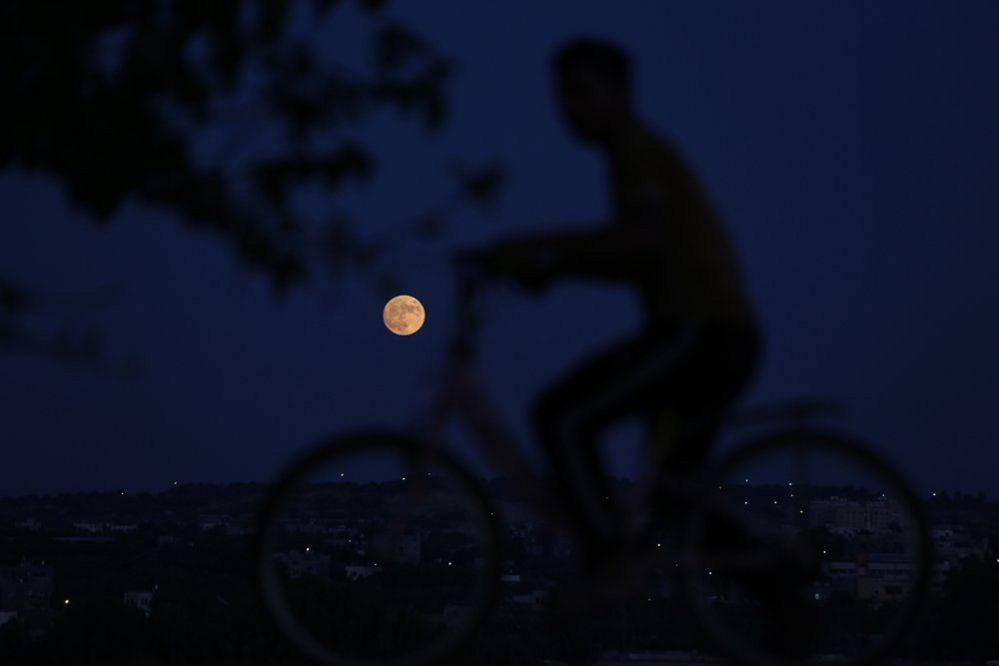 A Palestinian boy rides his bicycle looking at the moon the 'Blue Moon' in Beit Lahiya northern Gaza Strip on August 30, 2023