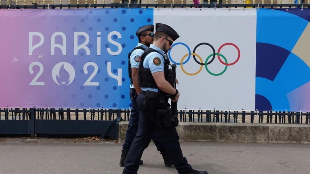 Police patrol a street near a poster advertising the Paris 2024 Olympic Games in Paris
