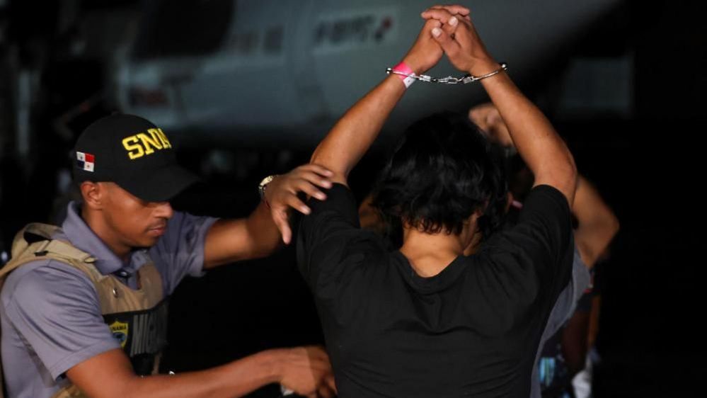 A Panamanian migration officer checks Colombian migrants who were detained after crossing into Panama irregularly through the dangerous Darien Gap, while they are handcuffed before boarding the first U.S. funded repatriation flight, at Tocumen International Airport, in Panama City, Panama August 20, 2024.