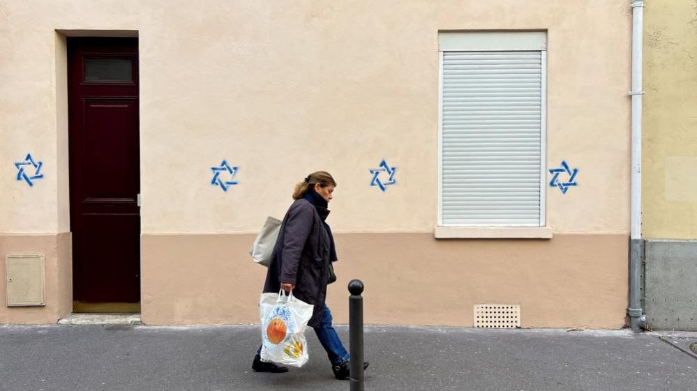 A woman walks past a building tagged with Stars of David in Paris