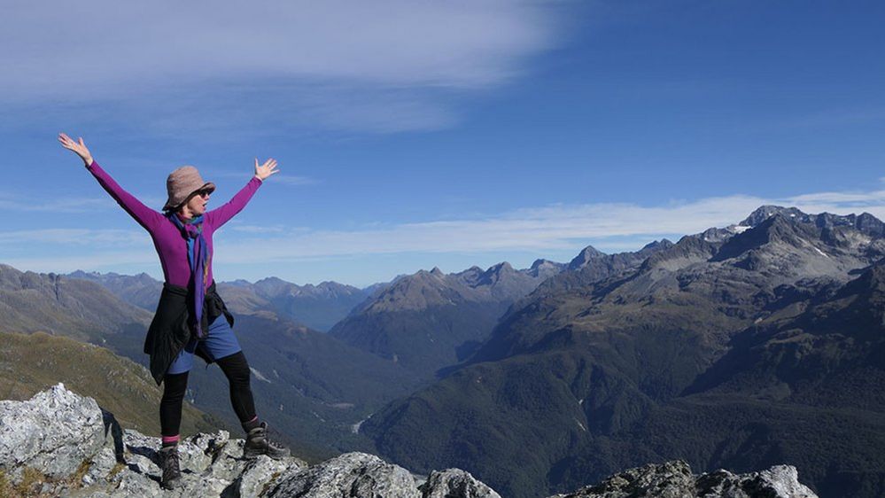 Woman raising her arms at the top of a mountain, in New Zealand
