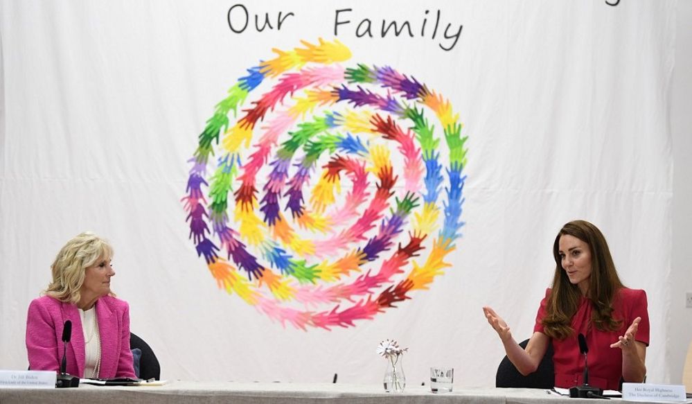 The First Lady sits socially distanced with the duchess, in front of a mural of multicoloured handprints