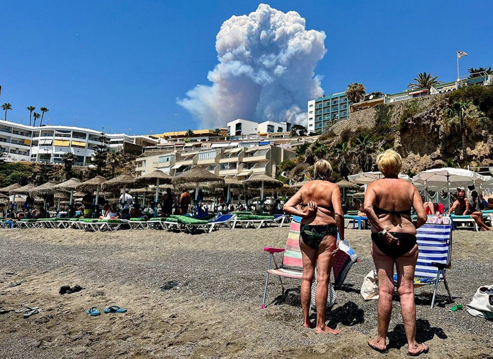 People look at plumes of smoke caused by a wildfire in Malaga, seen from Playa del Bajondillo beach in Torremolinos, Spain, 15 July 2022.