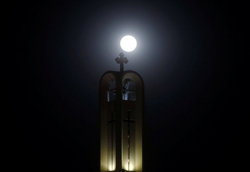 The moon rises behind The cross of St Antony Church