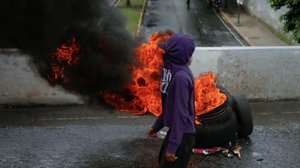 youth stands next to burning tyre in caracas