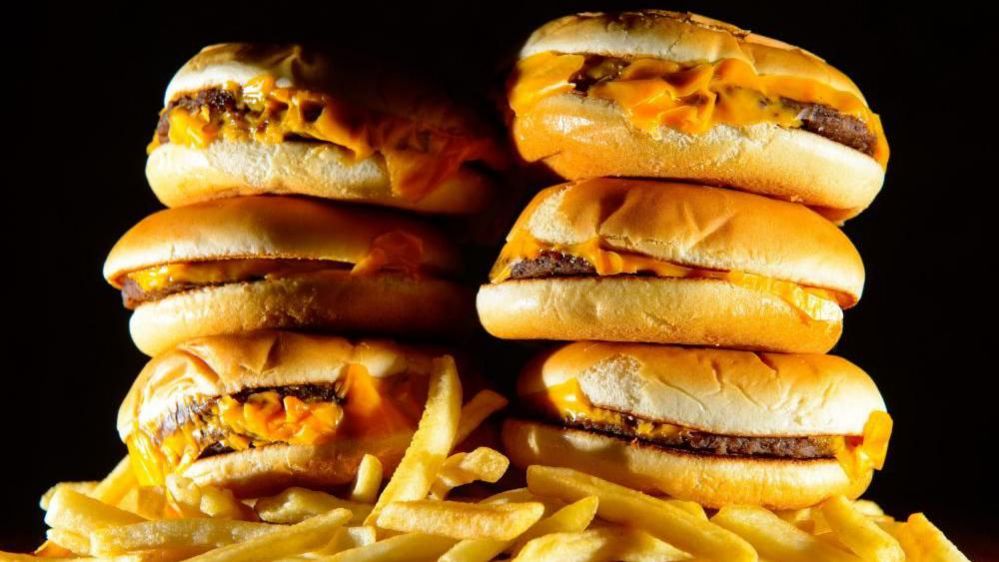 A pile of cheese burgers sit on top of chips. 