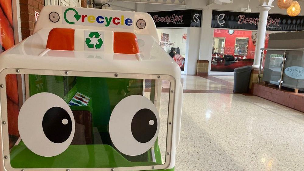 A child's ride-on recycling truck ride with a shop in the background 