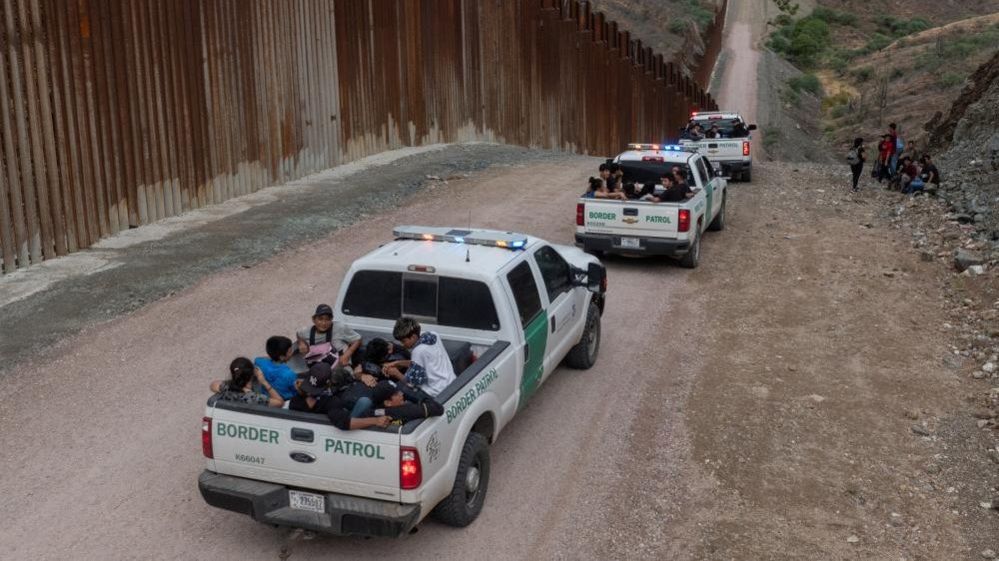 Border Patrol trucks drive along the US-Mexico border
