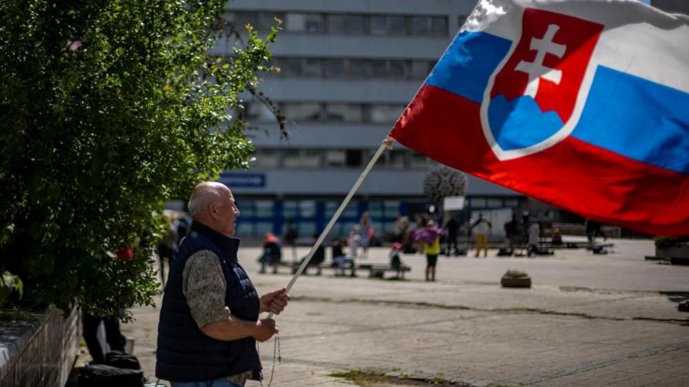 man waves slovak flag outside the hospital