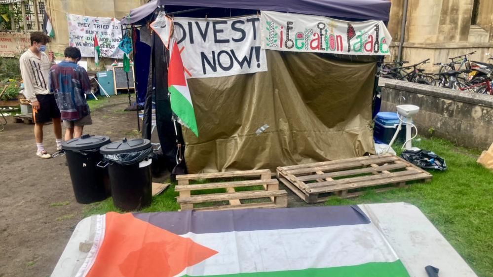 Two demonstrators stand outside a makeshift shelter at the Gaza war protest camp in Cambridge