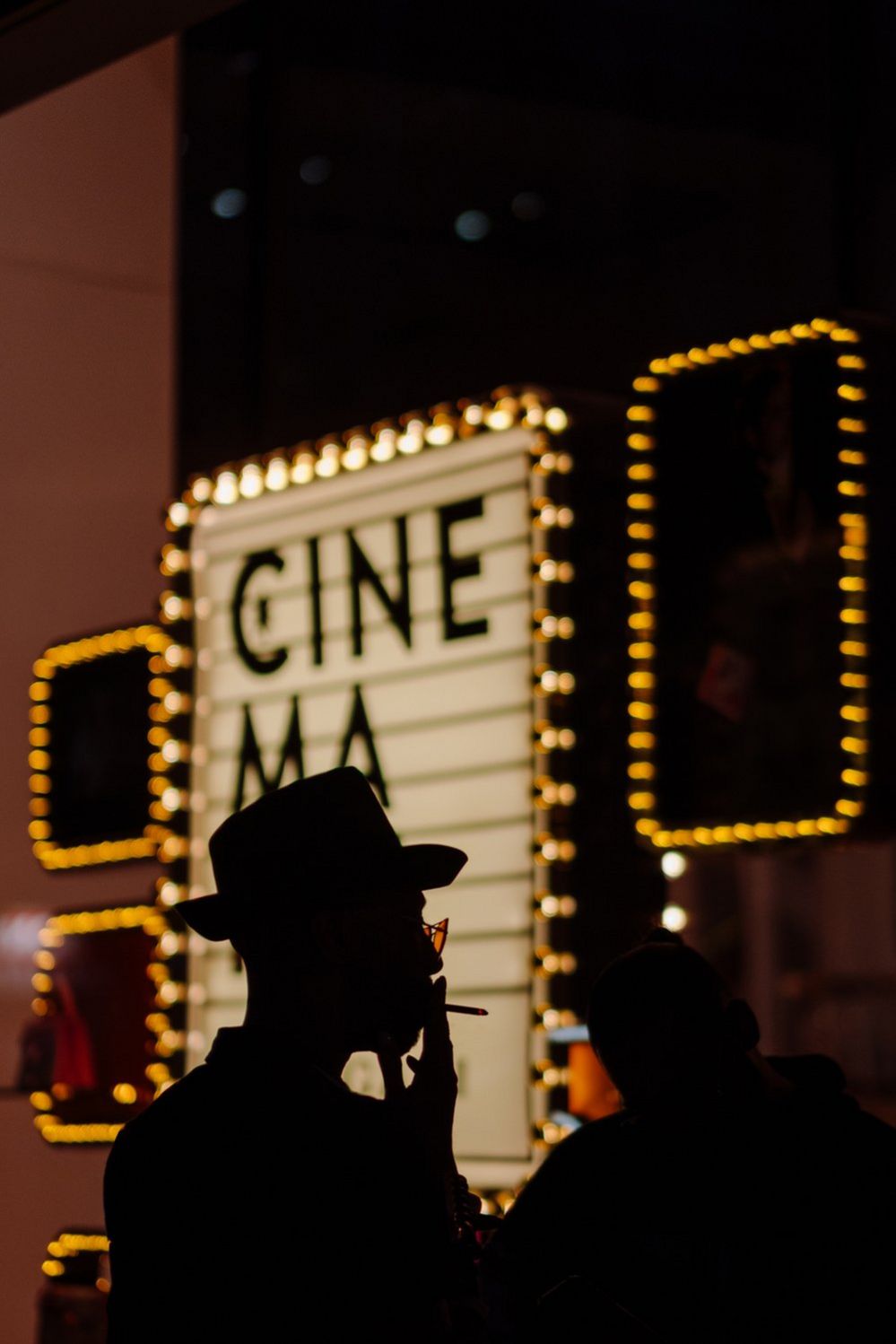 Silhouette of a person holding a cigarette in front of a cinema sign