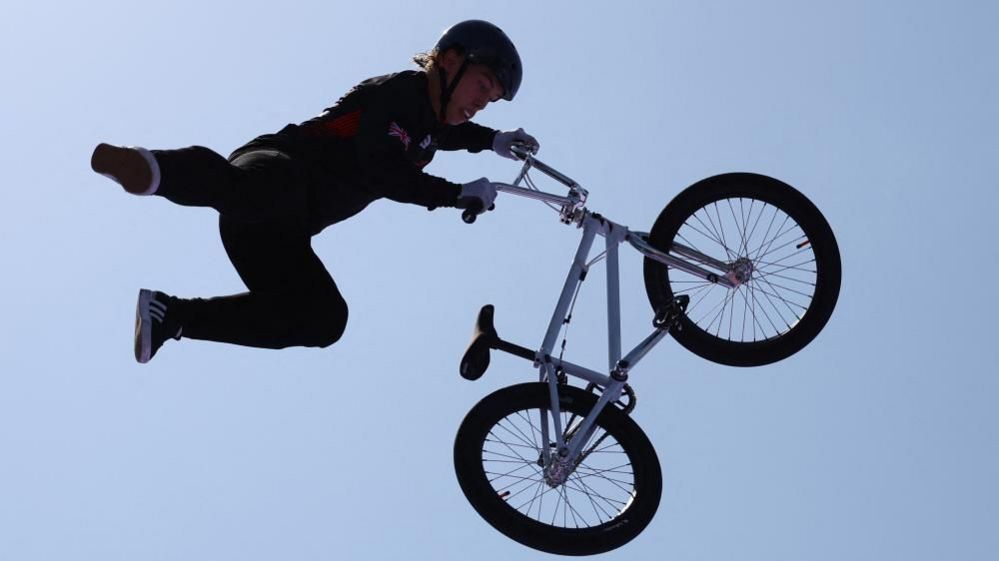 Reilly in black holding onto the handlebars of his airborne bike