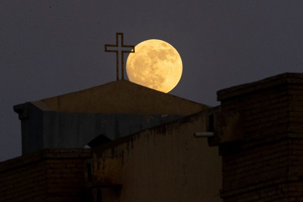 The moon nears the end of its waxing gibbous phase as it rises above the Virgin Mary Chaldean Cathedral in Iraq's Basra city, on July 2, 2023