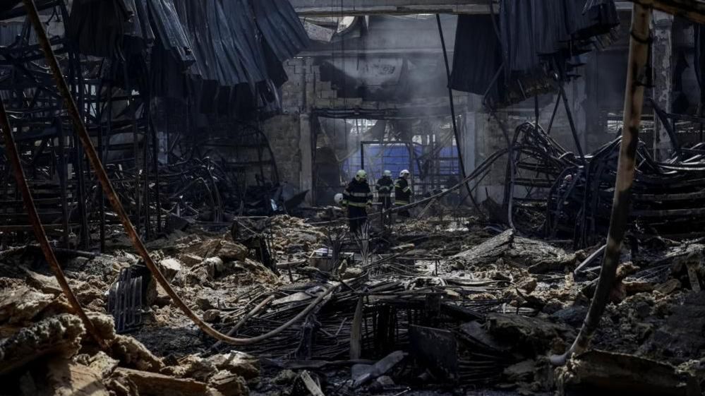 Firefighters work at a site of a shopping mall hit by yesterday's Russian airstrike