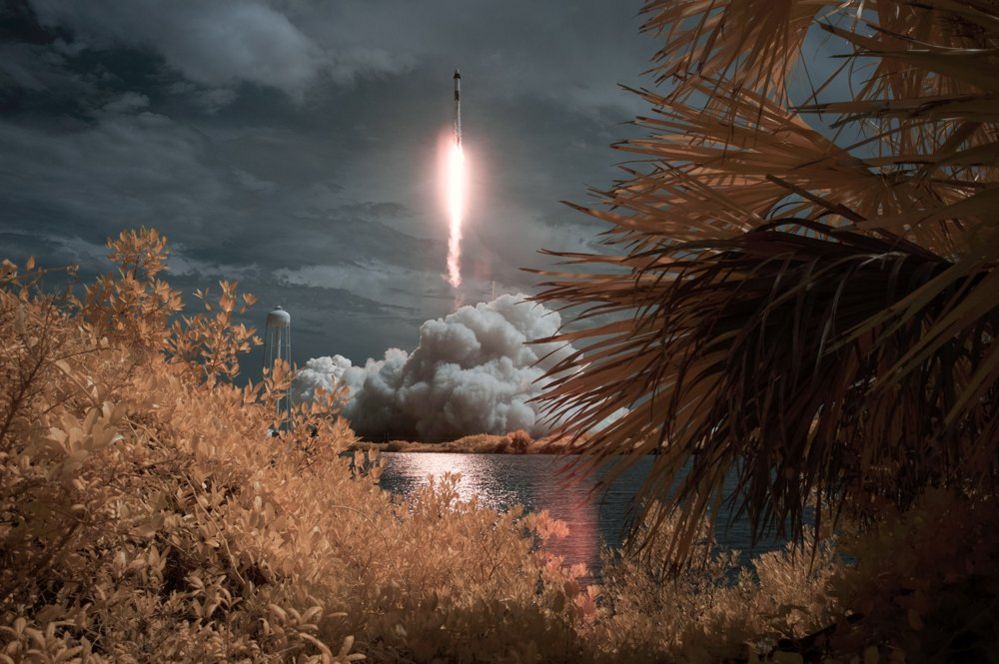 A SpaceX Falcon 9 rocket carrying the Crew Dragon spacecraft launches in the distance