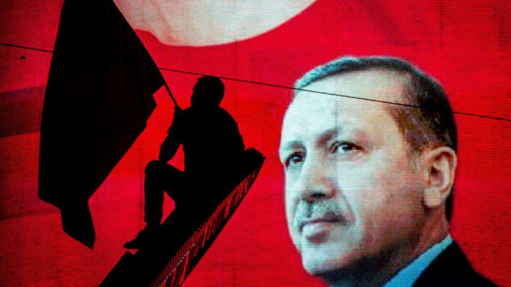 Supporter of Turkish President Recep Tayyip Erdogan waves flag against electronic poster during rally in Ankara on July 18, 2016