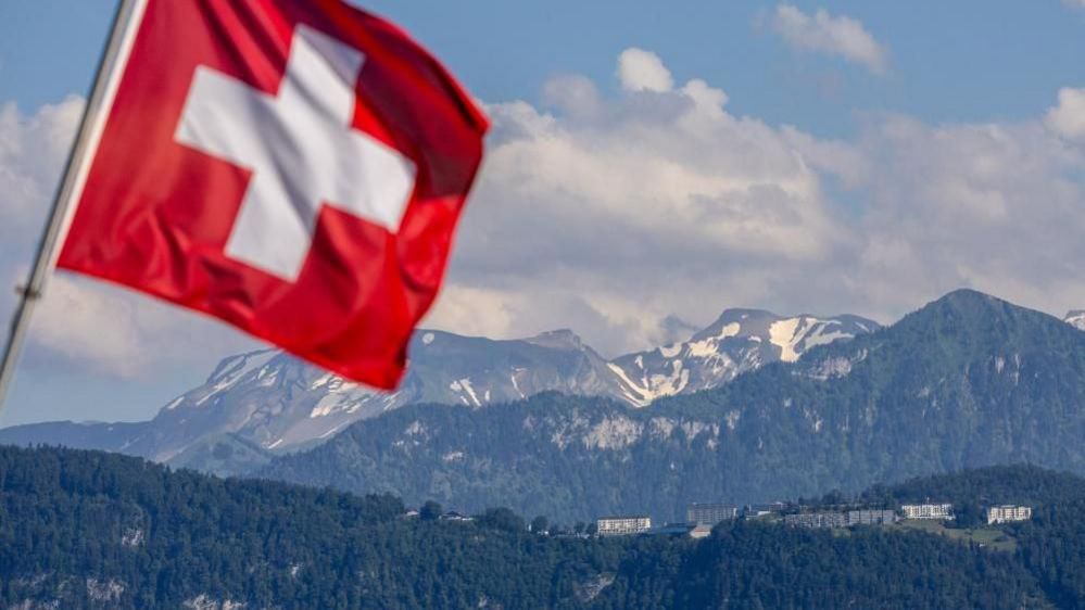 The Swiss flag flies in front of a view of snow-capped mountains and the hotel where the peace summit took place in Lucerne, Switzerland