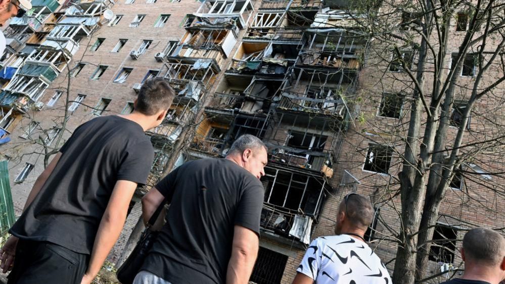 People gather in the courtyard of a multi-storey residential building, which according to local authorities was hit by debris from a destroyed Ukrainian missile, in the course of Russia-Ukraine conflict in Kursk