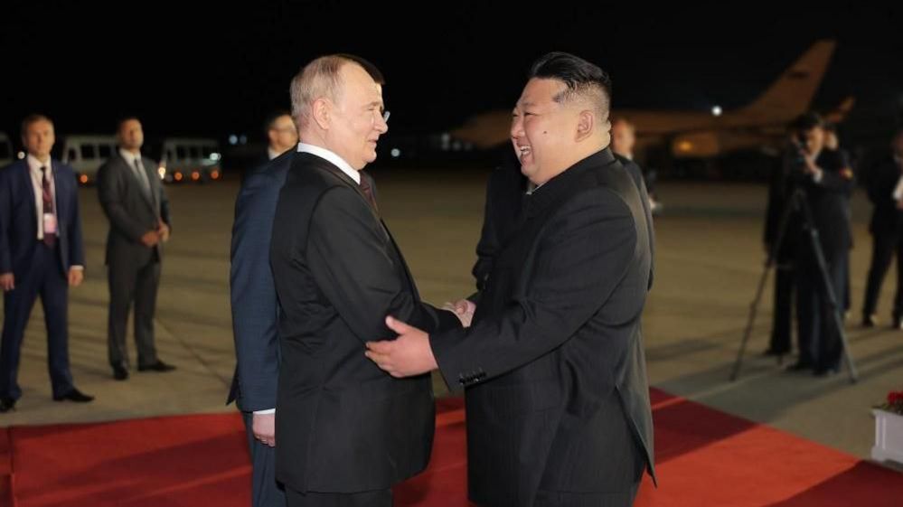 Russian President Vladimir Putin and North Korean leader Kim Jong Un smile as they greet one another with a handshake on the airport runway, decked with a red carpet, in Pyongyang