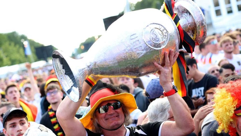 A Germany fan holds up a fake Euro trophy