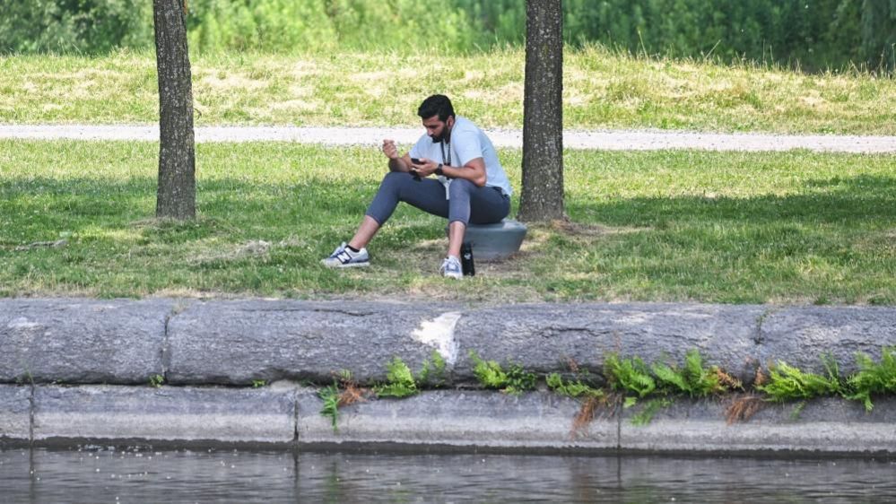 A man sits in shade next to a canal in Montreal, Canada