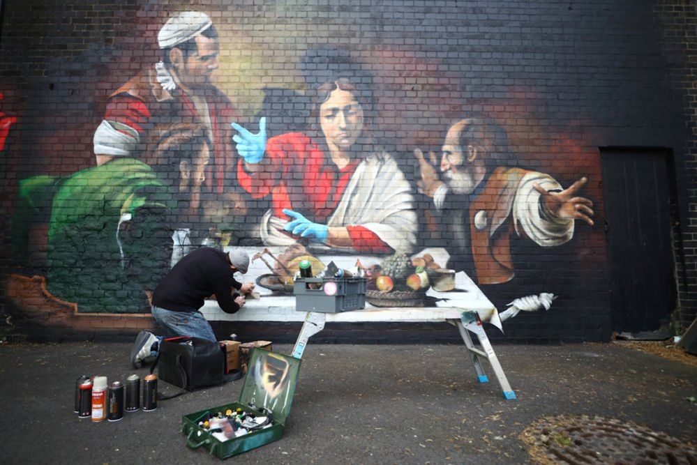 An artist paints a mural depicting the Supper at Emmaus by Caravaggio