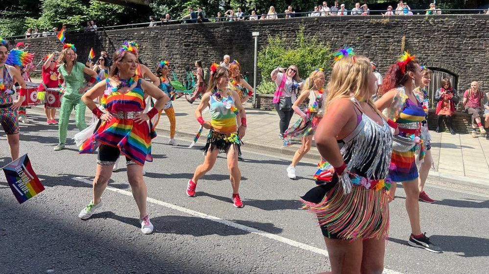 People dressed in rainbow and sparkly outfits dancing in the street