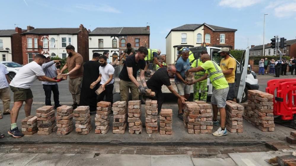 Members of the community in Southport working together to rebuild a wall damaged after a protest in Southport