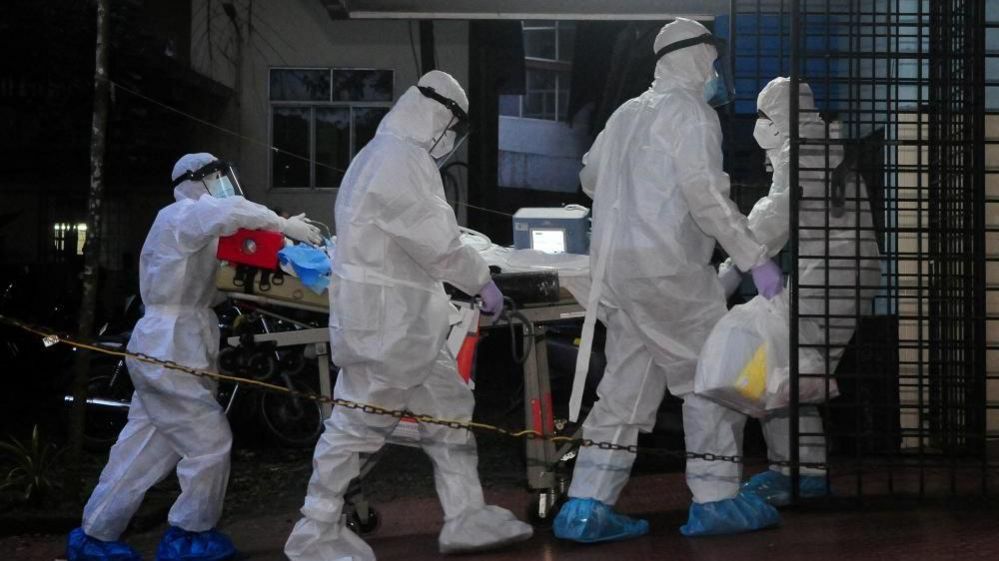 A patient with Nipah Virus is transferred in hospital - a group of people in personal protection gear are pushing them on a stretcher