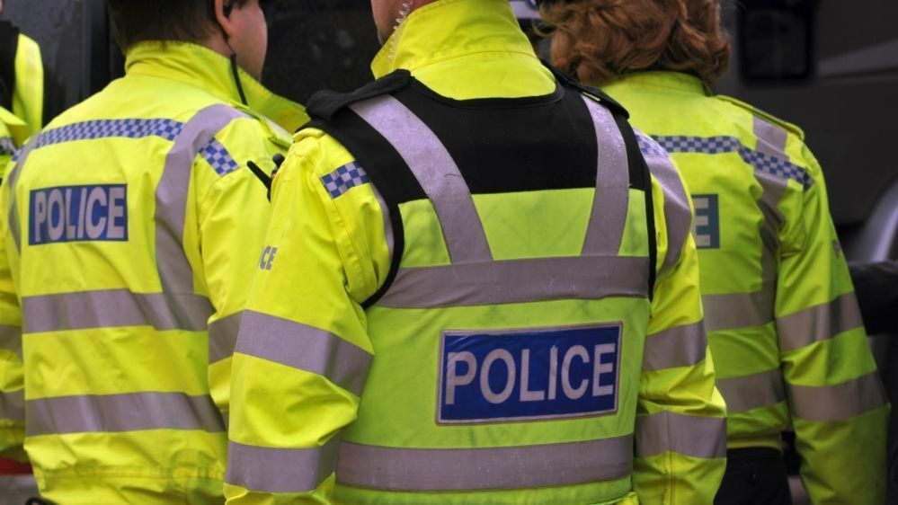 The back of police officers in bright yellow police jackets