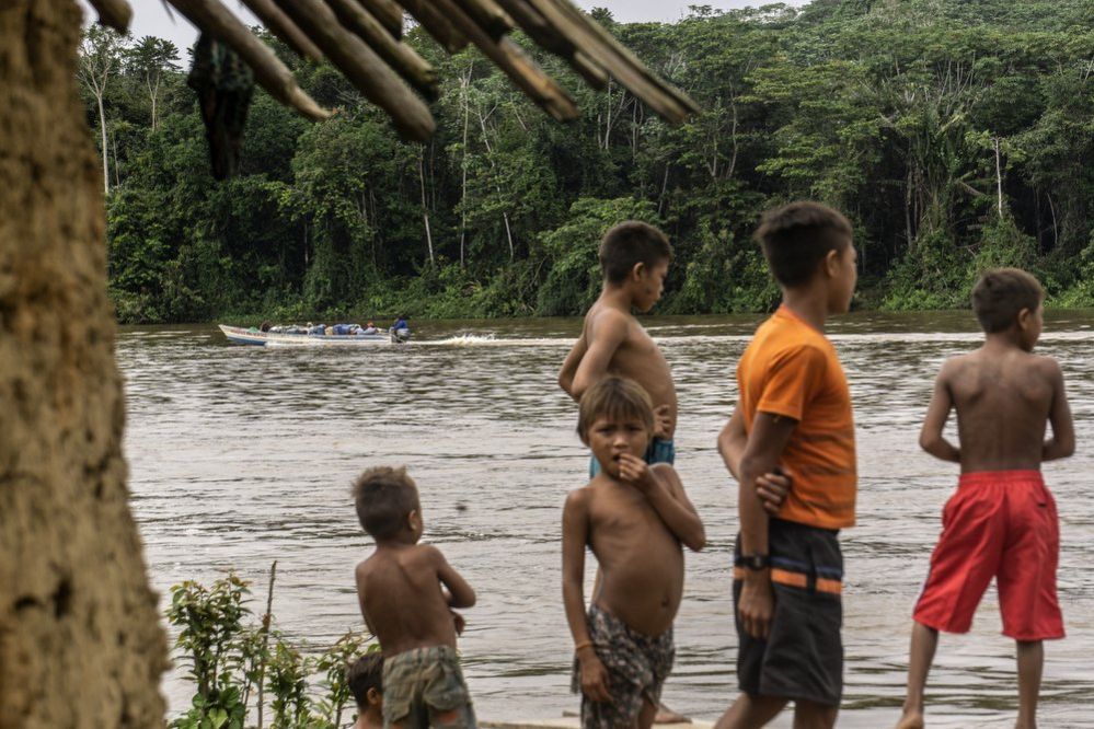 Children watch a boat go past on the river in the Waikas community