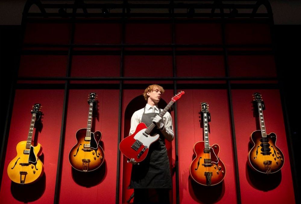 A Christie's art handler holds up Mark Knopfler's Red Schecter Telecaster guitar at Christie's in London