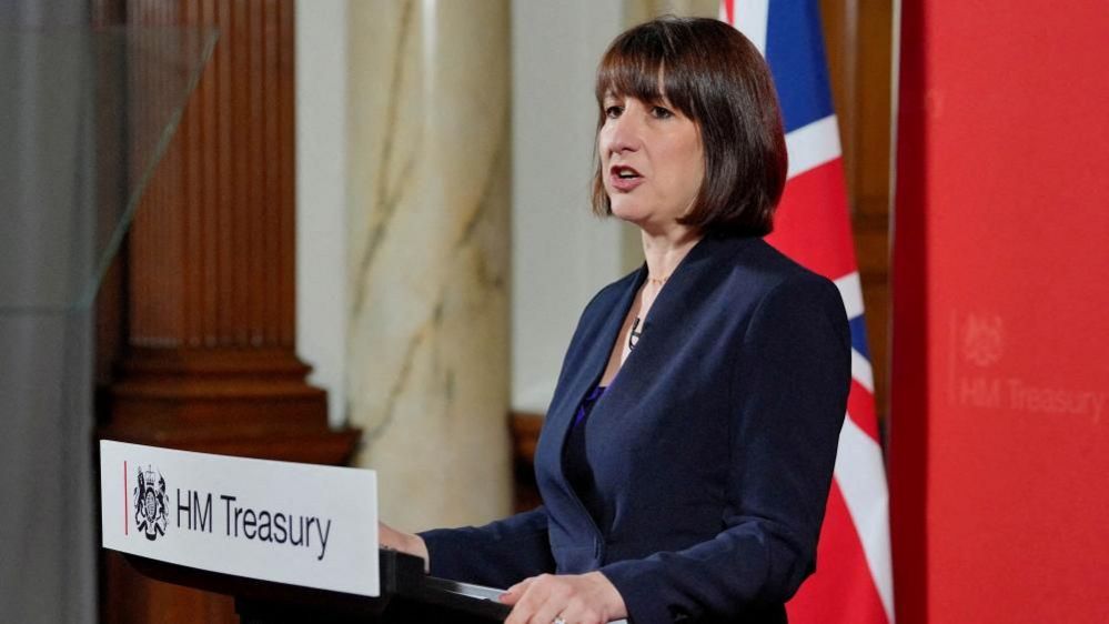 Rachel Reeves speaking at a conference with dark hair and blue jacket