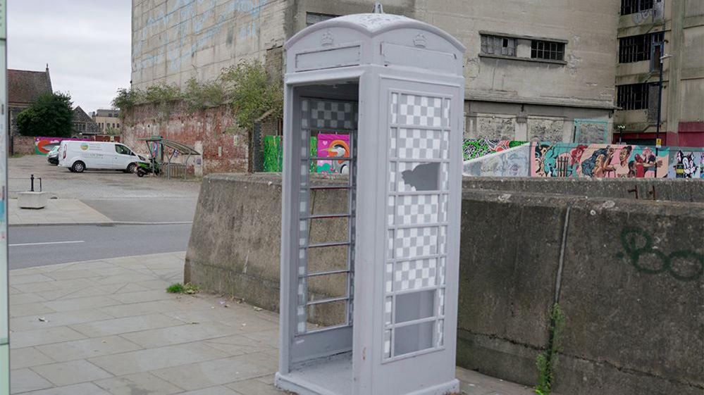 A telephone box in Ipswich painted grey with a chequered paint design over its class windows.