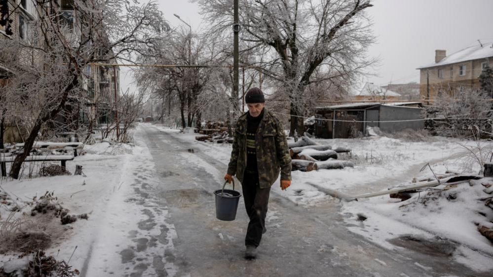 Man carries water through snow-covered Ukrainian street