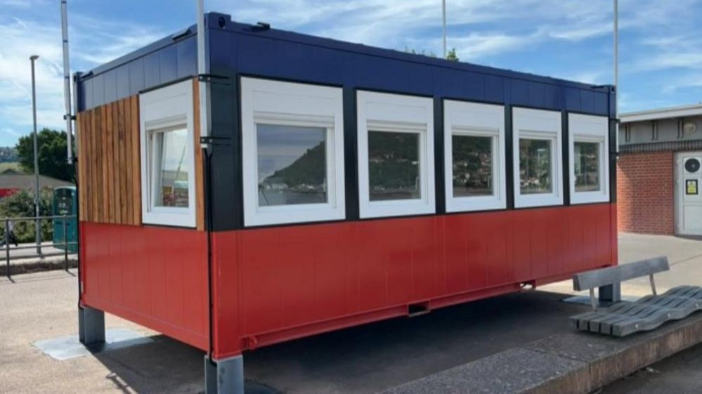 The new Coastwatch station building on Minehead seafront. It is small building, raised slightly off the ground. It has white windows and is painted red and blue.