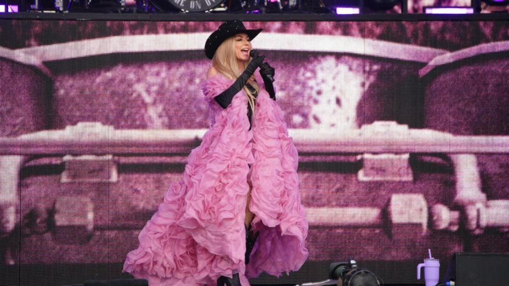Shania Twain wearing a large pink overcoat on stage singing