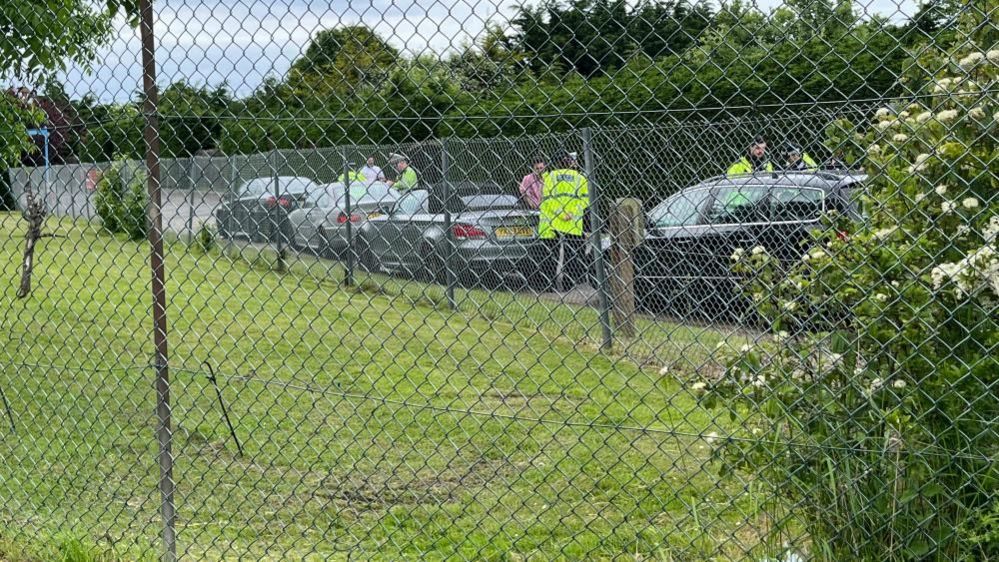 Cars pulled over by police with drivers being interviewed, with a fence partially obscuring the view